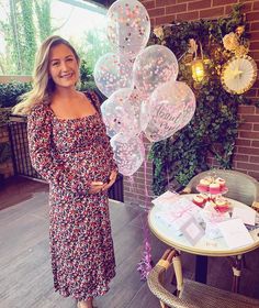 a pregnant woman standing in front of a table with balloons and cupcakes on it