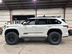 a white suv parked in a garage next to another vehicle with large tires on it