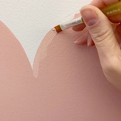 a person is painting a heart on the wall with a paint roller and a marker