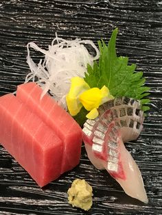 two pieces of sushi sit next to each other on a black surface with yellow flowers