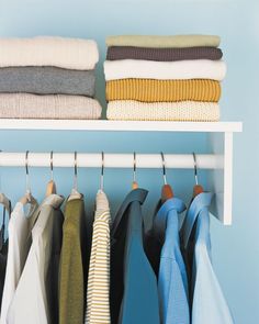 an organized closet with folded clothes and folded sweaters on hangers, against a blue wall