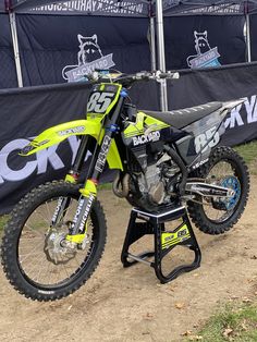 a yellow and black dirt bike parked on top of a dirt road next to a sign