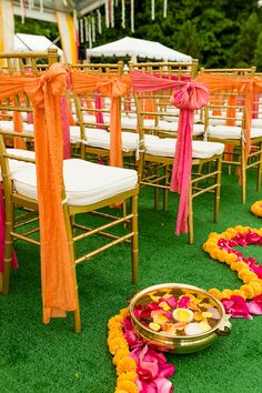 rows of chairs with orange sashes and pink flowers on the grass at an outdoor ceremony