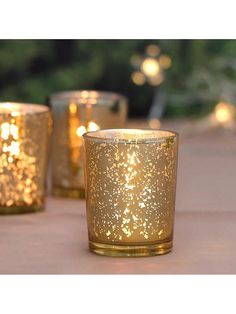 three lit candles sitting on top of a table next to each other with trees in the background