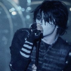 a man with black hair holding a microphone in his hand and wearing a leather jacket