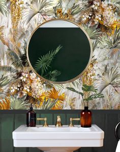 a bathroom sink sitting under a mirror in front of a wallpapered wall with palm leaves