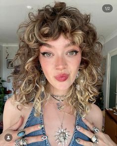 a woman with curly hair wearing rings and necklaces on her chest, making a funny face