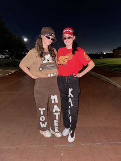 two young women standing next to each other on a brick walkway at night with their arms around each other