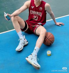 a young man sitting on the floor with a basketball and water bottle in his hand