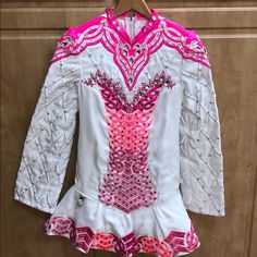 a white shirt with pink and silver designs on it's chest, hanging from a wooden hanger