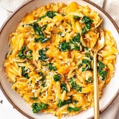 a bowl filled with pasta and spinach on top of a white table cloth next to a gold spoon