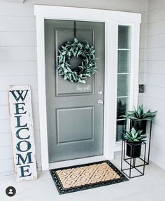 a front door with a welcome mat and potted plants