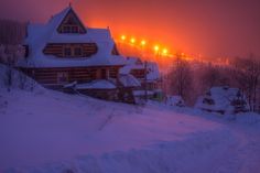 the sun is setting over a snowy mountain town with houses and trees in the foreground