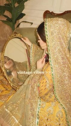 a woman sitting in front of a mirror wearing a yellow and green dress with gold trim