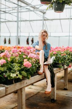 a woman sitting on a bench in a greenhouse reading a book while surrounded by flowers