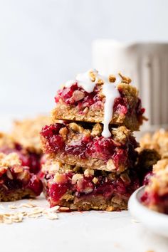 three berry crumbler bars stacked on top of each other next to a bowl of oatmeal