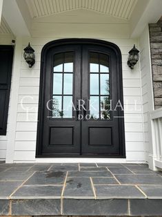 a black double door with two sidelights on the front of a white house that has stone steps leading up to it