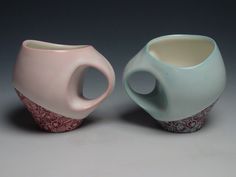 two vases sitting next to each other on a gray surface with white and pink designs