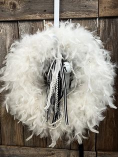 a white wreath with black and white feathers on a wooden door hanger in front of a wood paneled wall