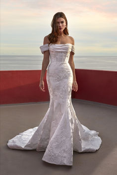 a woman in a white wedding dress standing on a balcony next to the ocean at sunset