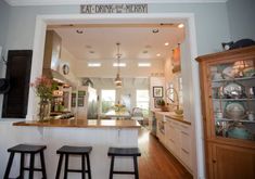 a kitchen with three stools in it and a bar area behind the counter that says eat drink be merry