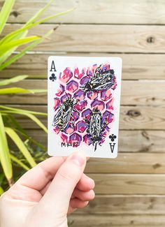 a person holding up a playing card in front of a wooden wall with plants on it