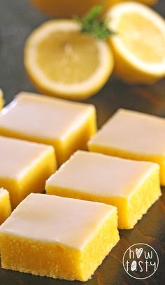 small squares of yellow cake sitting on top of a wooden table next to sliced lemons