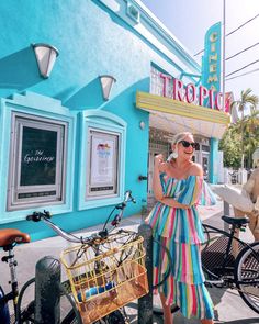 a woman standing in front of a blue building with a bike parked next to it