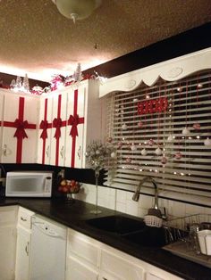 a kitchen decorated for christmas with red and white bows on the window sill, microwave and sink