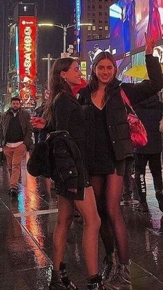 two women standing in the middle of a city street at night with umbrellas on