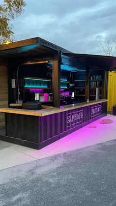 an outdoor bar is lit up with purple lights and sits next to a yellow fence