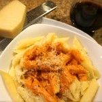 pasta with cheese and sauce in a white bowl next to a glass of red wine