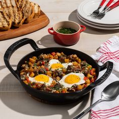 a skillet filled with eggs on top of a table next to toasted bread