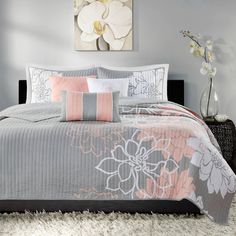 a bed with grey and pink comforter set on top of a white carpeted floor