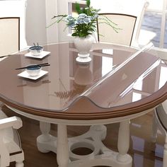 a glass table with white chairs and a vase filled with flowers on top of it