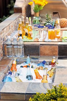 an outdoor bbq with bottles and glasses on the grill area, surrounded by potted plants