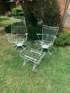 two metal chairs sitting in the grass next to a tree