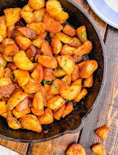 a skillet filled with fried potatoes on top of a wooden table next to plates