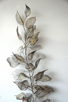 a metal branch with leaves on it against a white wall