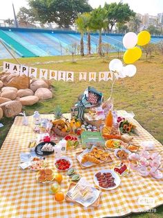 an outdoor picnic with food and balloons on the grass in front of a swimming pool