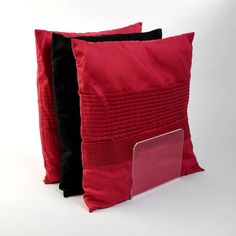 two red and black pillows sitting next to each other on a white surface with a laptop in the middle