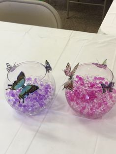 two glass bowls filled with pink and purple flowers on top of a white table cloth