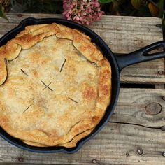 a pie in a cast iron skillet on a wooden bench with flowers behind it