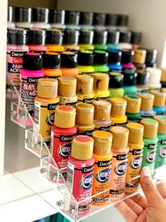 someone is holding up some paint bottles in front of a wall full of other colors