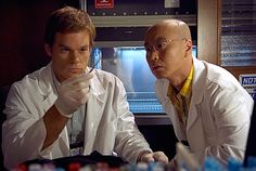 two men in lab coats look at something on the table