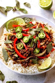 a white bowl filled with rice, meat and veggies next to sliced limes