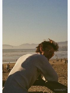 a man sitting on top of a bench next to the ocean with people in the background