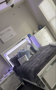 a bed with blue and white pillows in a bedroom next to a dresser under a chandelier