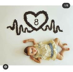 a baby laying on the ground in front of a heart made out of coffee beans