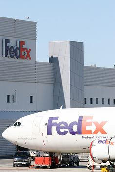 a fedex airplane parked in front of an airport terminal with cars and trucks around it